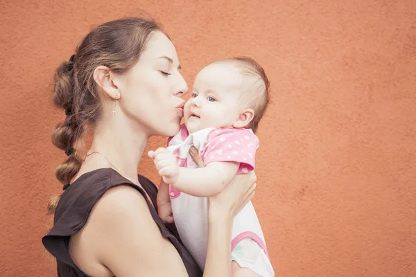 Happy mother kissing her baby at wall background