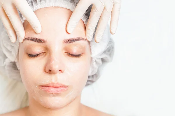 Woman in spa salon receiving face treatment with facial cream