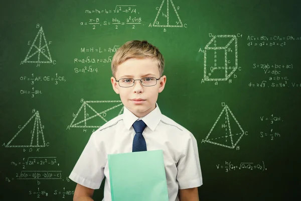 Smart student or schoolboy with a notebook standing near blackboard