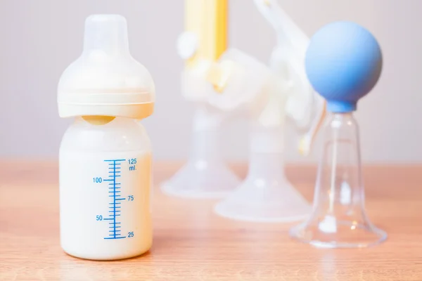 Baby bottle with milk and manual breast pump at background