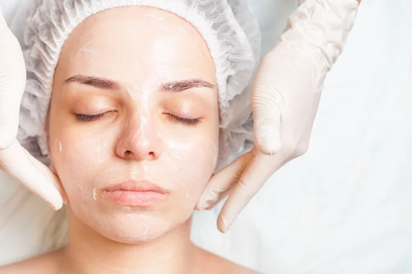 Woman in spa salon receiving face treatment with facial cream