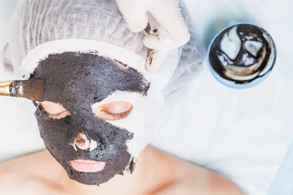 Professional woman, cosmetologist in spa salon applying mud face mask