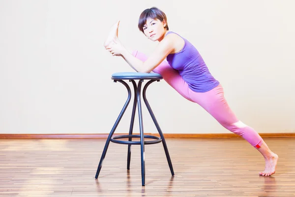 Asian woman stretching for yoga exercise at home by chairs