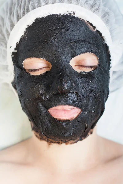 Woman in spa salon with black mud face mask