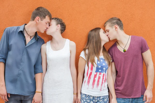 Small group of people kissing, standing near red wall background