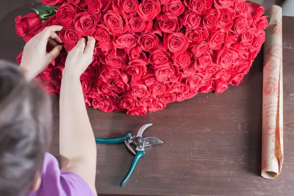 Florist woman prepares a big bouquet of red roses