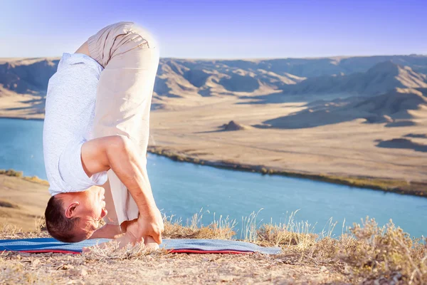 Man doing exercise of yoga outdoor above river valley