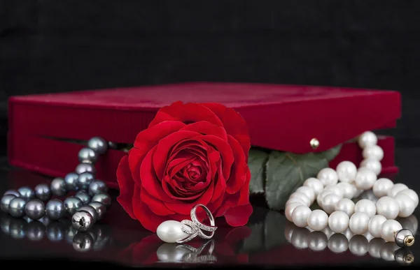 Butterfly ring , pearl necklace , red rose on black background