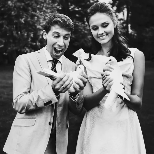 Happy smiling bride and groom holding white doves on a sunny day