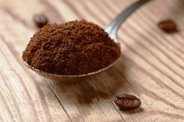 Spoon of ground coffee and coffee beans on wooden table, low angle view with shallow depth of field
