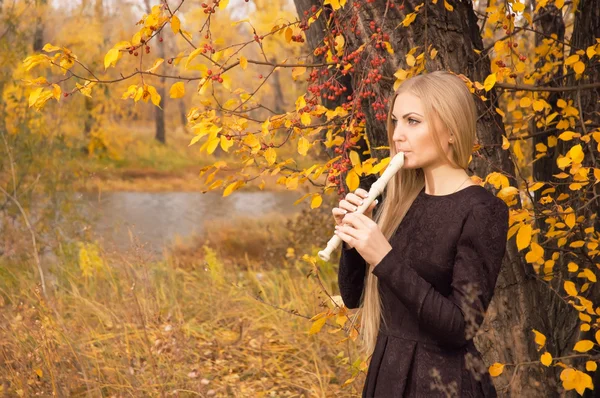 Beautiful young blonde woman playing flute recorder in autumn forest
