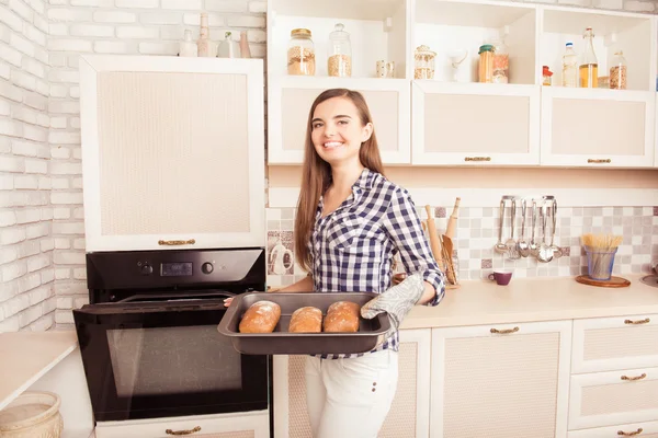 Pretty young woman taking an oven-tray with baked bread from ove