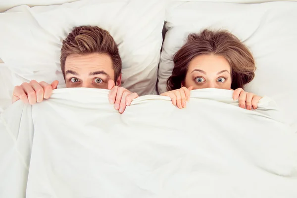 Surprised funny couple in love lying in the bed hiding themselve