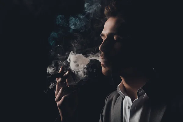 Handome cheeky man in suit on the black background smoking a cig