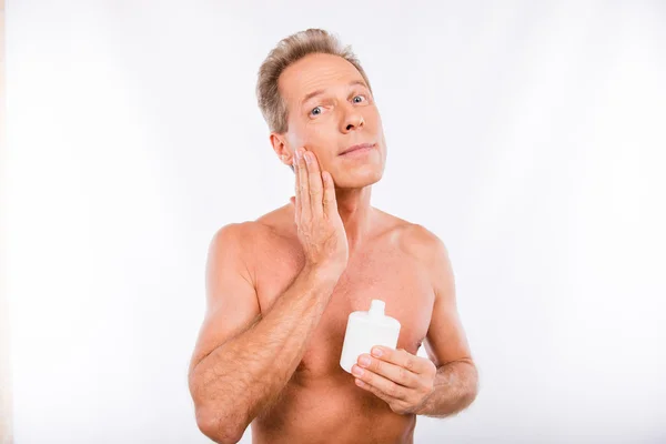Handsome shaved aged man holding a bottle of lotion and smearing