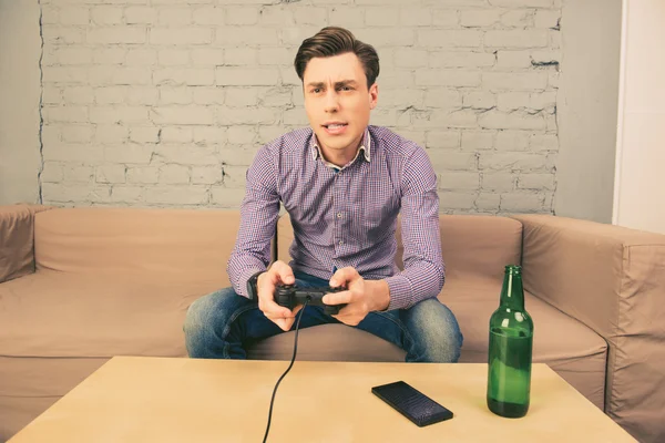 Young man sitting on couch and playing video games with beer