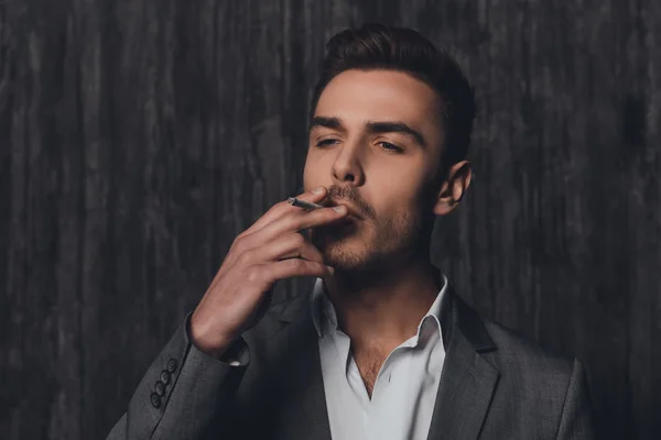 Handome brutal man in suit on the gray background smoking a ciga