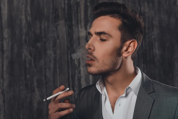 Side view of a cheeky man in suit on the grey background smoking