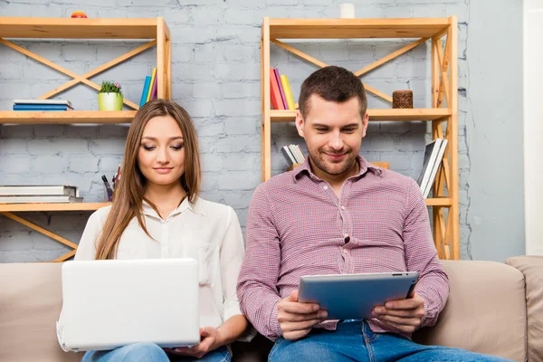 Excited man and woman sitting on couch with laptop and tablet
