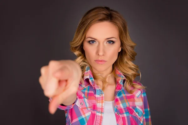 Challenge! Strict young woman pointing on camera on gray backgro