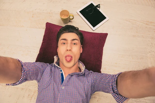 Pretty man lying on the floor and making selfie with tongue