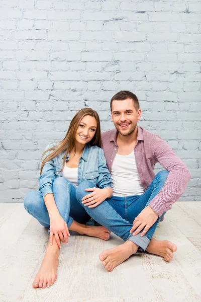 Two cheerful lovers sitting barefoot on the floor and huging