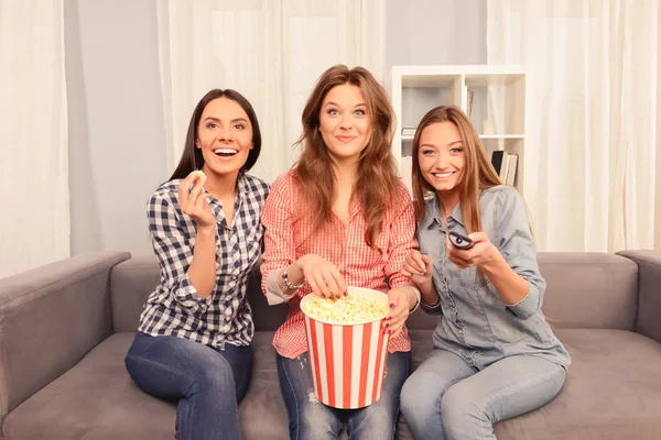 Three excited beautiful girls watching film and eating popcorn