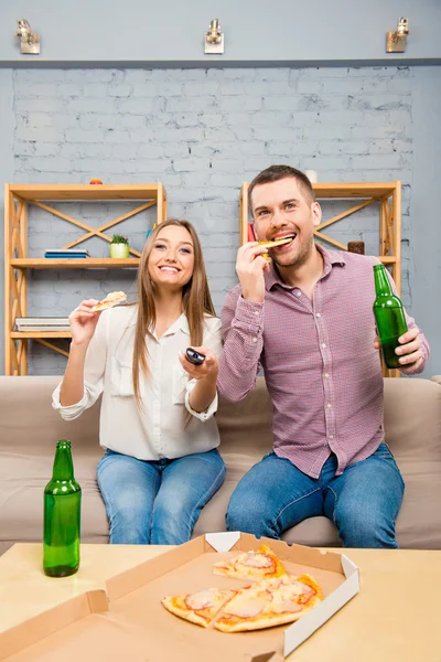 Excited young couple watching film with beer and pizza