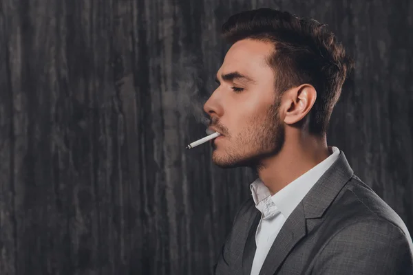 Side view portrait of handsome man in suit smoking a cigarette