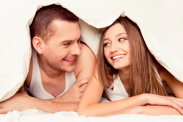 Cute happy man and woman lying in bed under blanket
