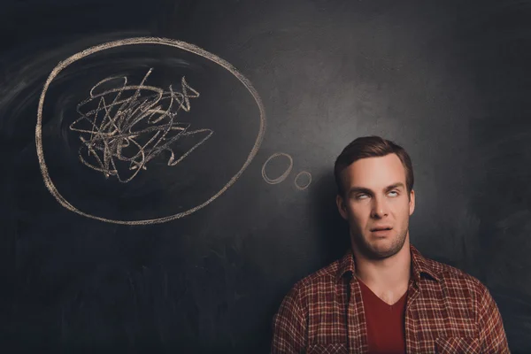 Young freelancer at a loss on the background of chalkboard