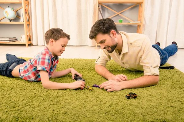 Father and son  lying on carpet and playing with toy cars