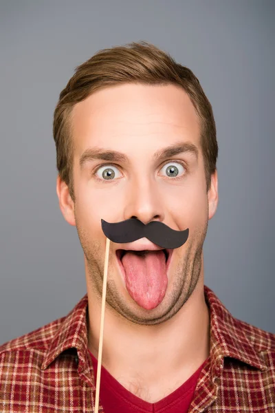 Close up photo of man with paper mustache showing tongue