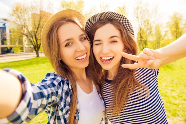 Two pretty girls making selfie, gesturing with two fingers and s