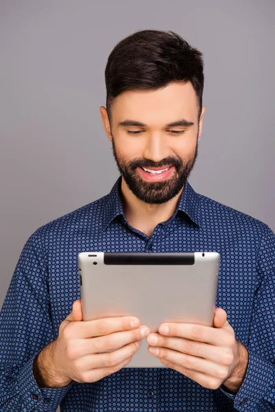 Attractive smiling young businessman holding tablet on gray back