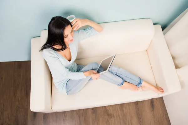 Top view of young woman sitting on couch and using tablet