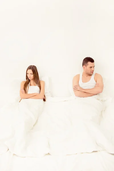 Young depressed couple sitting in bed after quarrel