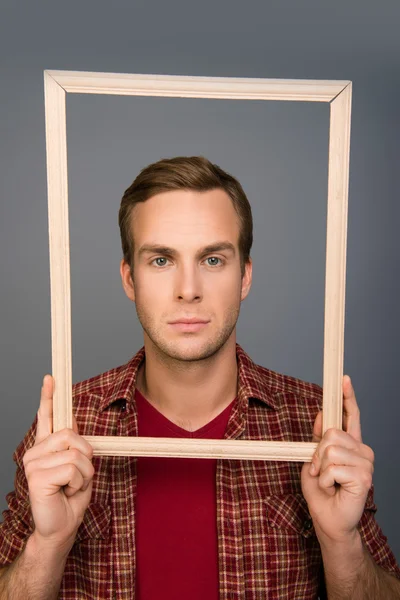 Portrait of serious minded man with frame in his hands