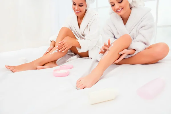 Portrait of two happy smiling girls applying cream on their legs