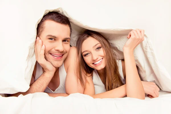 Happy pretty man and woman lying under blanket in morning