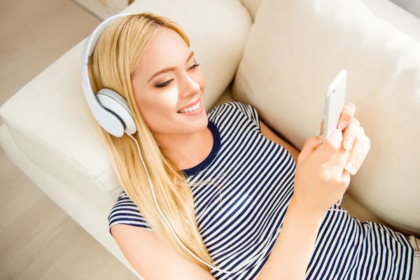 Portrait of beautiful girl lying on couch and listening music in