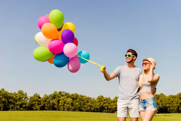 Happy man and woman in glasses walking with color balloons