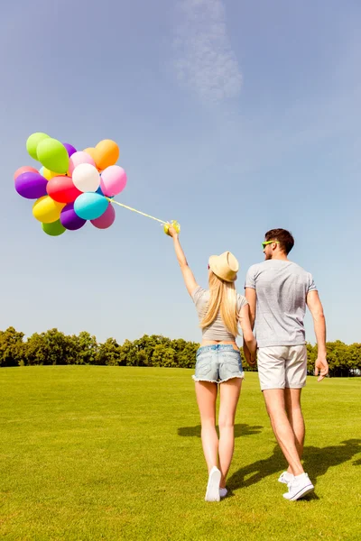 Back view of two friends walking in park with balloons