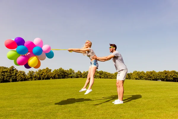 Happy man catching his girlfriend not to fly with balloons