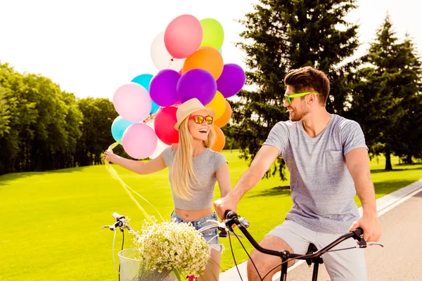 Happy positive young couple on bicycle in a summer park with bal