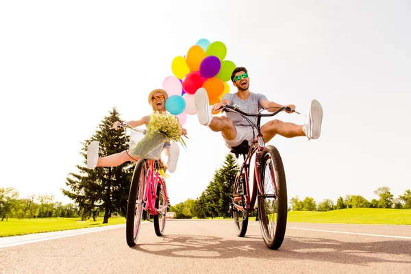 Happy funny young couple riding on bicycle with raised legs