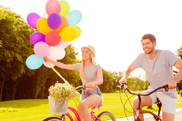 Portrait of two happy lovers riding bicycles with balloons