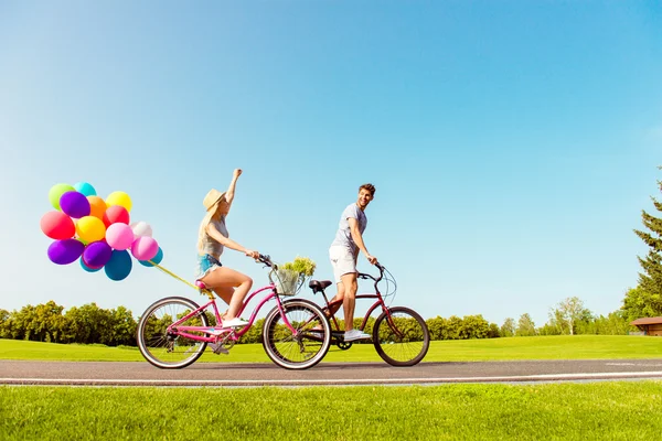 Two lovers riding bicycles with balloons on the background of sk