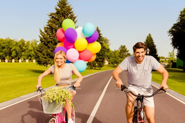 Happy couple in love riding a bicycle race with balloons in park