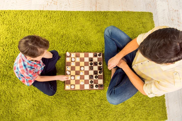 Top view of father and son sitting on carpet and playing chess